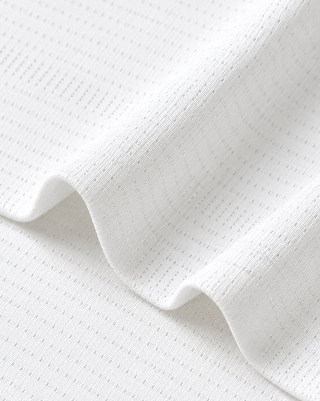 White textured T-shirt knit Reference illustration: Close-up of white fabric with a fine dotted knit texture and a curved folded edge.